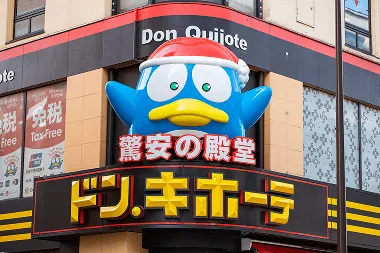 Don Quijote shopping mall entrance featuring a blue penguin mascot wearing a Christmas hat, welcoming visitors with holiday cheer in Japan