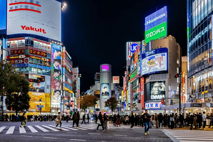 The iconic Shibuya Scramble Crossing with thousands of pedestrians navigating the world’s busiest intersection, framed by towering high-end malls and vibrant billboards illuminating the lively streets of Tokyo in the night