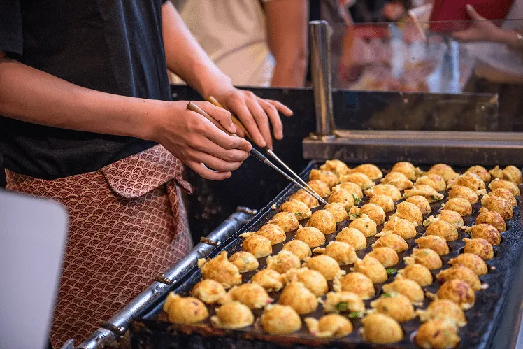 Takoyaki, savory, round snacks made from a wheat flour-based batter cooked in a special molded pan, giving them their iconic golf ball shape