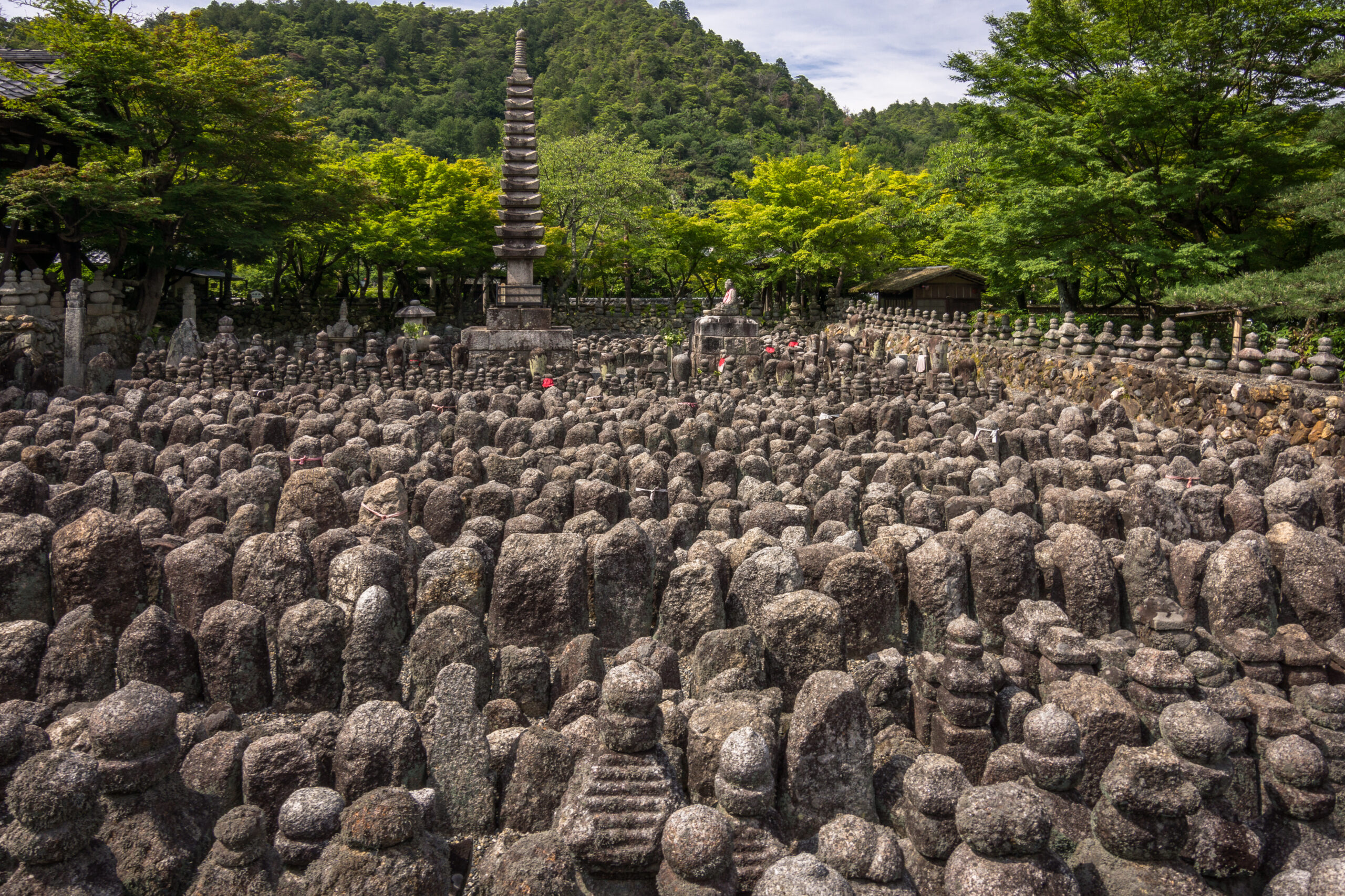 Hundreds of ancient stone statues and a tall pagoda stand together in a tranquil memorial garden surrounded by lush greenery in Kyoto, Japan