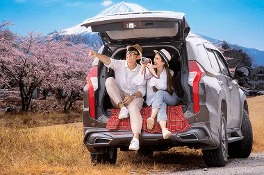 A couple enjoying their spring vacation in Japan, seated together in a rental car, surrounded by blooming cherry blossoms