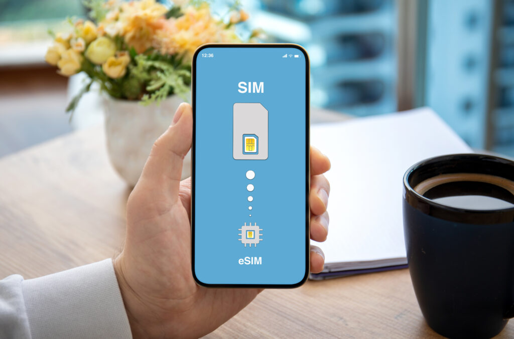 A man is holding a smartphone that displays both the Physical SIM﻿ and eSIM﻿ symbols on its screen, illustrating the coexistence of the two SIM technologies