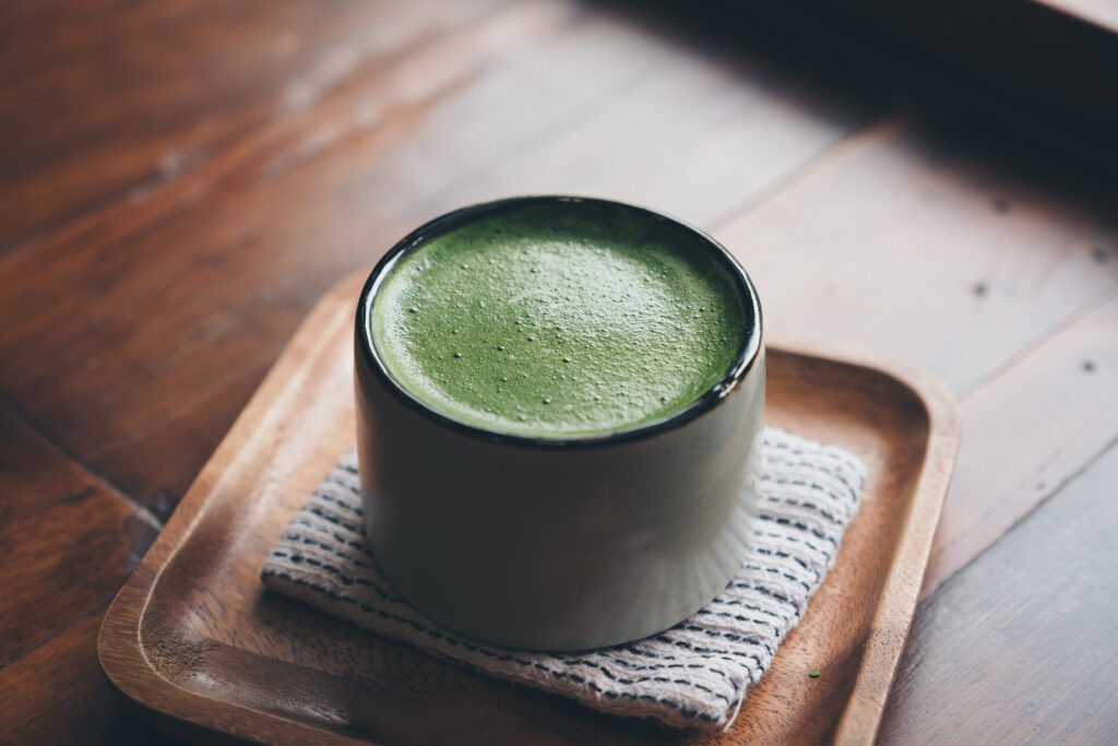A cup of vibrant green matcha latte sits on a soft cloth coaster, placed neatly on a small, rustic brown square tray