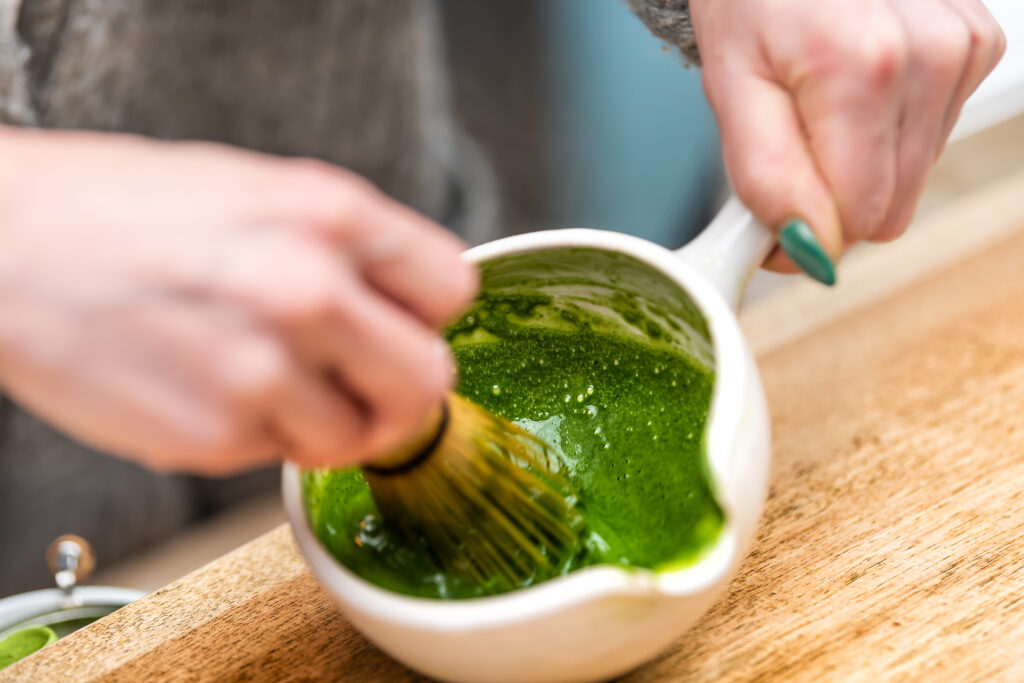A woman gracefully whisks bright green matcha powder in a tea bowl, creating a deep, vibrant foam during a hands-on Japanese tea ceremony