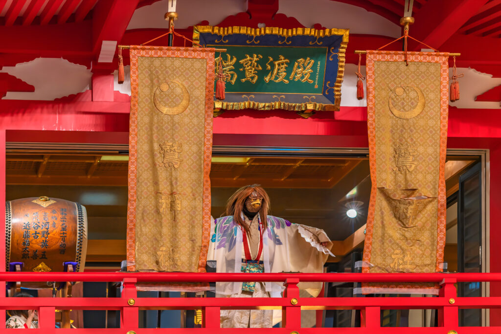 Japanese dancer in a kimono wearing a rooster mask performs a graceful kagura dance with a fan at Ootori Shrine during the lively Tori-no-Ichi festival