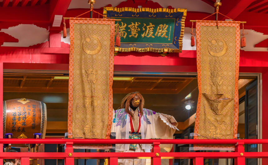 Japanese dancer in a kimono wearing a rooster mask performs a graceful kagura dance with a fan at Ootori Shrine during the lively Tori-no-Ichi festival
