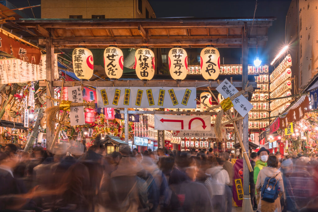 Crowds pass through a street adorned with glowing lanterns at the Tori-no-Ichi Festival in Ootori Shrine, where traders purchase auspicious bamboo rakes believed to bring success in business