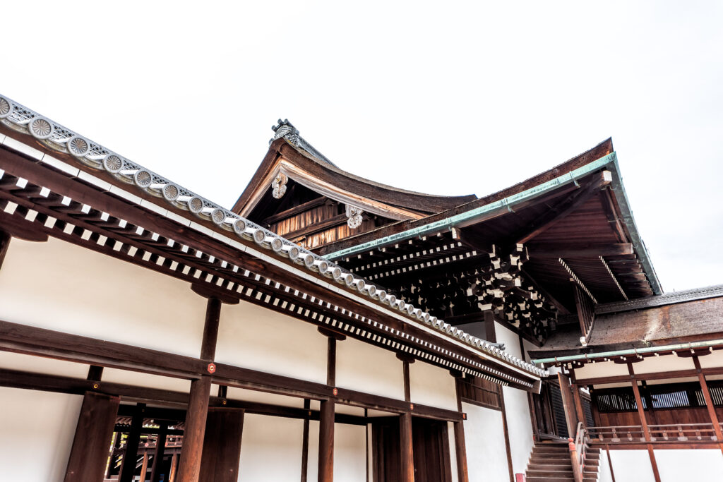 Close-up view of the Kyoto Imperial Palace's architectural details, showcasing polished wooden steps leading to the entrance and intricate carvings on the pillars and beams of the Shishinden hall, under bright sunlight