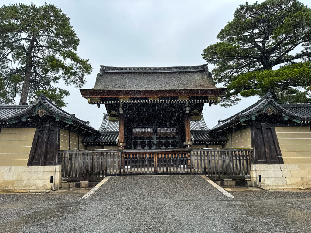 View of the Kyoto Imperial Palace's Kenreimon Gate from Kyoto Gyoen National Garden on a rainy day, with misty atmosphere enveloping the historic wooden architecture