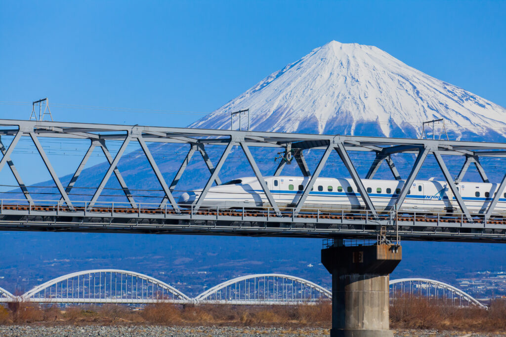A high-speed Shinkansen train darts swiftly like a jet on its route over a bridge, framed spectacularly by the majestic Mount Fuji in the background