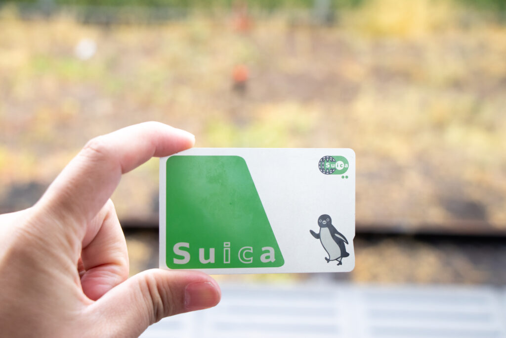 A woman is holding a green Suica IC card featuring a cute penguin