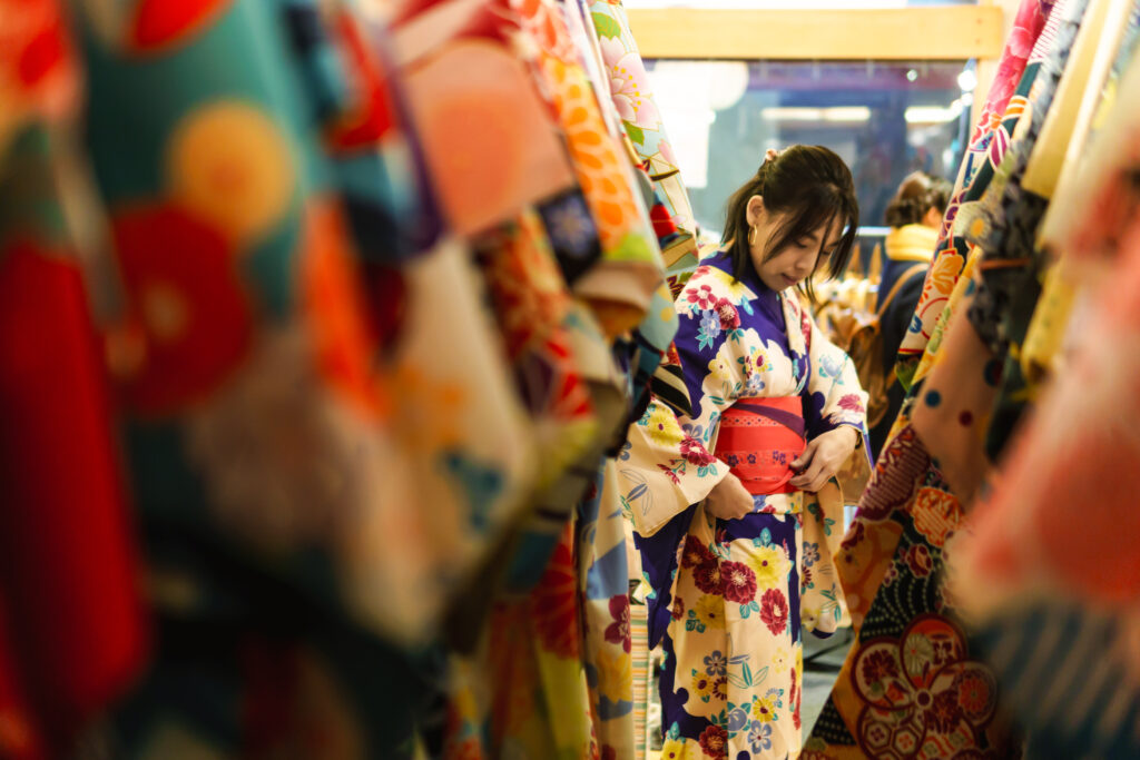 A joyful woman stands in a cozy Kyoto kimono rental shop, excitedly trying on vibrant traditional kimonos during her cultural travel adventure